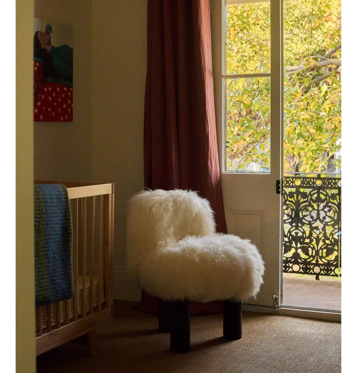 A plush white chair and crib rest on luxuriously crafted natural fibre flooring in a serene, light-filled nursery opening to leafy views.
