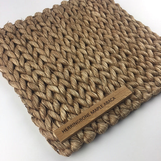 A herringbone-patterned maple abaca mat featuring thick, natural fibers and a small wooden label, styled in an elegant interior.