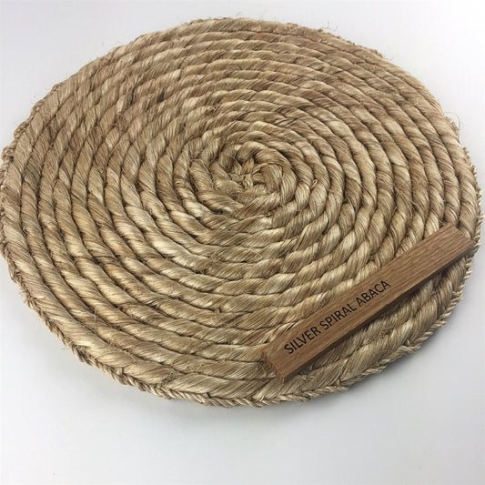 A round, tightly woven silver mat in an intricate spiral pattern, crafted from natural abaca for a refined, sustainable look.