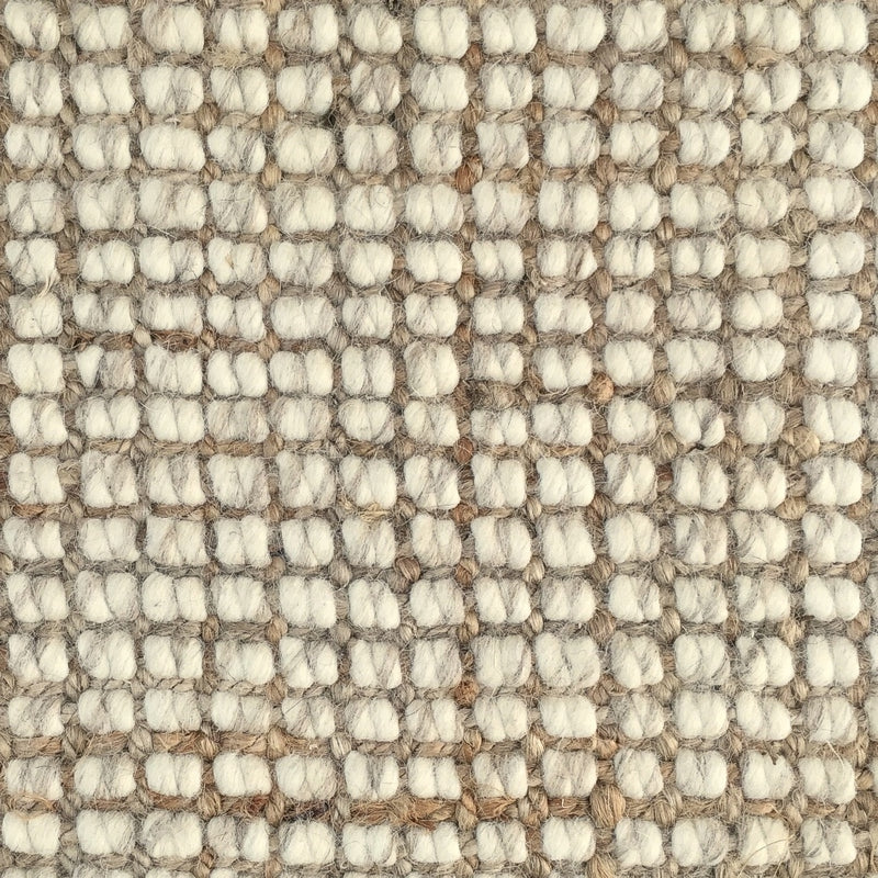 Detail of a wool and jute floor covering with a subtle grid pattern and thick, hand-crafted textured loops in soft natural tones.